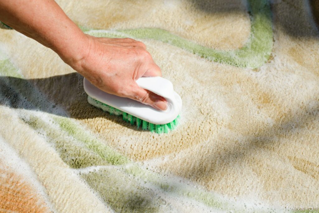 Carpet cleaning with brush and detergent foam. Close-up of woman's hand cleaning wet rug. Home