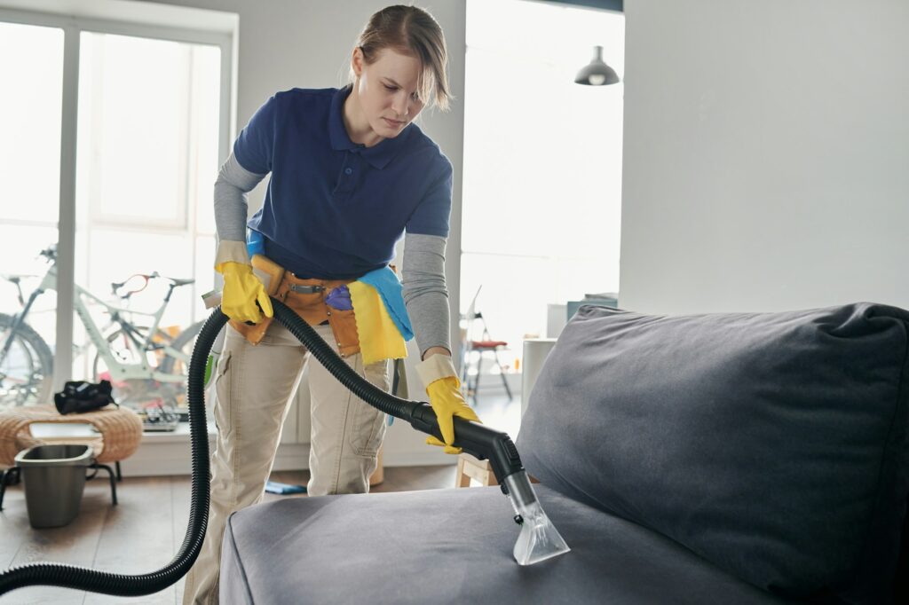 Cleaning service worker vacuuming the sofa