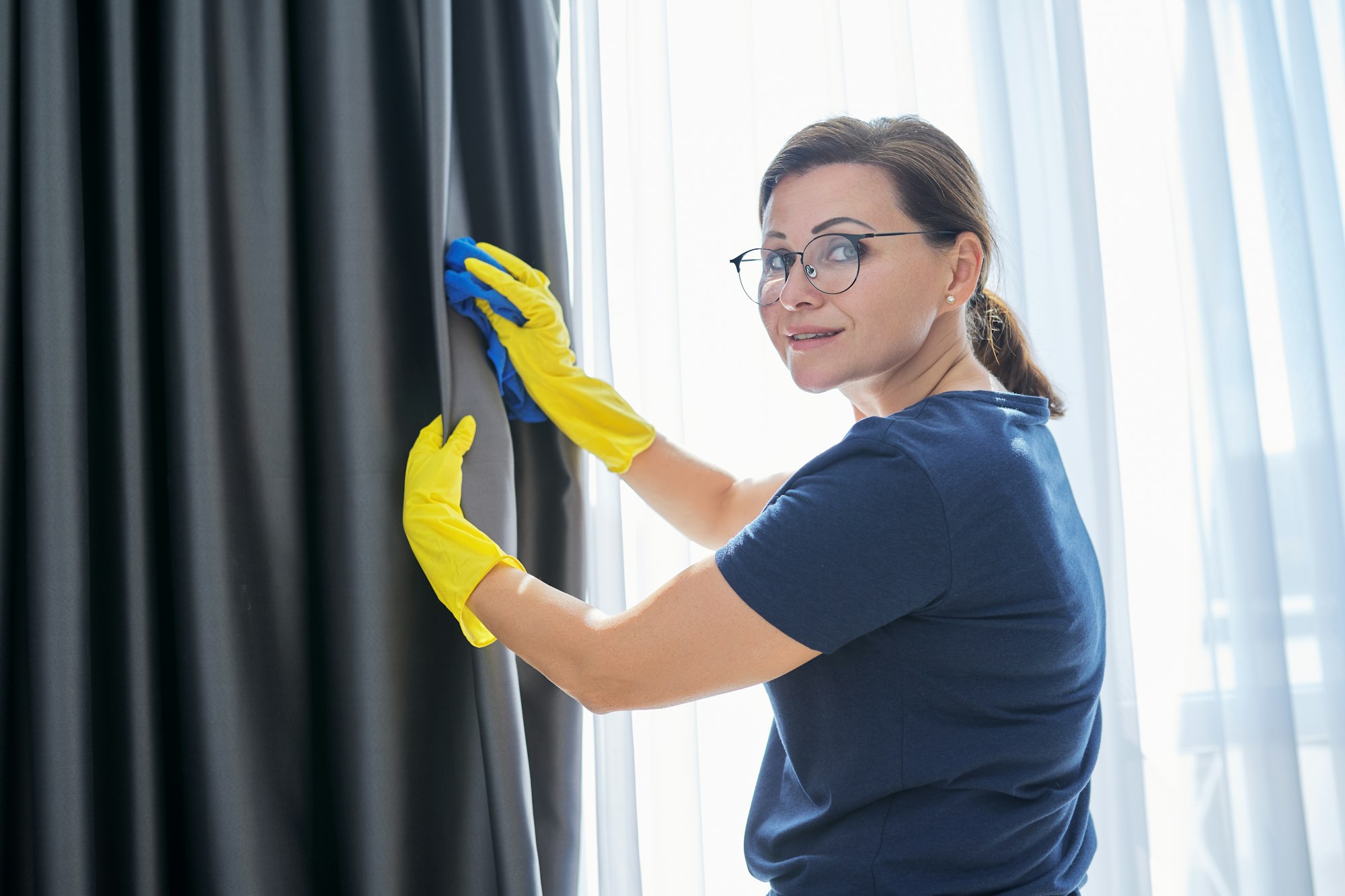 House cleaning, woman in gloves with a rag cleaning curtains